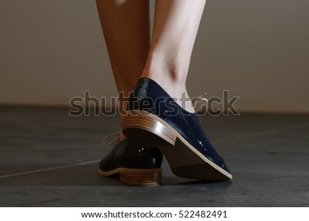 Closeup photo of patent-leather female shoes with laces. Walking, back view.