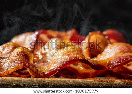 Closeup photo of a pile of freshly cooked hot crispy bacon resting on a wood cutting board