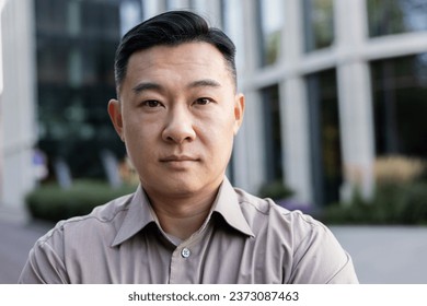 Close-up photo. Portrait of a young Asian man in a shirt standing outside on the street and looking seriously at the camera. - Powered by Shutterstock