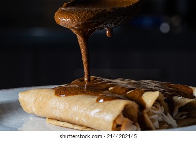 Closeup Photo Of The Preparation Of Typical Mexican Food. Mole Enchiladas. Fried Tortillas With Chicken Inside And Mole Sauce On Top.