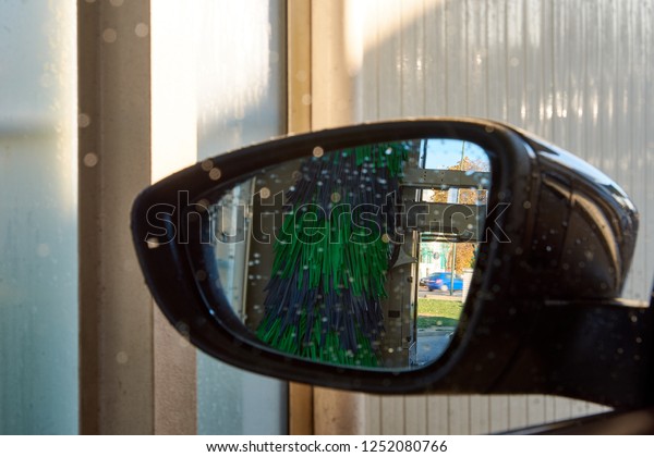 Close-up photo of a rear-view mirror inside a car\
wash with water drops
