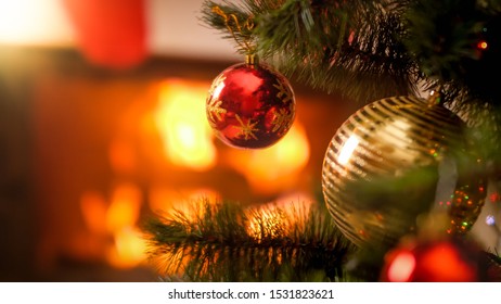 Closeup Photo Of Red And Golden Xmas Baubles Hanging On Christmas Tree Aginst Burning Fire In Fireplace