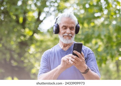 Close-up photo of senior smiling gray-haired man standing, walking in park, doing sports in headphones and chatting on mobile phone. - Powered by Shutterstock