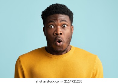 Closeup photo of shocked handsome millennial black man with eyes and mouth wide open looking at camera, african american guy showing emotions amazement on blue studio background