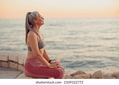 Close-up photo of sporty female sitting on the edge of shore with her eyes closed, relaxing - Powered by Shutterstock