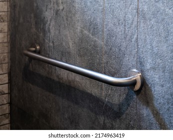Close-up photo of stainless steel grab bar handrail installed on grey stone tiles wall background in a hotel handicapped disabled access bathroom. - Shutterstock ID 2174963419