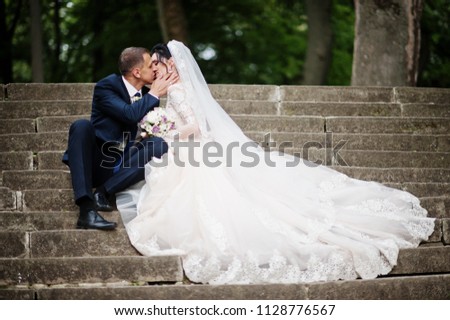 Close-up photo of wedding couple sitting and kissing in the park. 