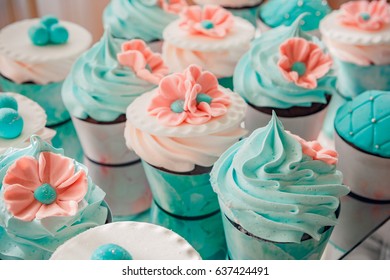 Close-up photo of wedding cupcakes placed on a glass stand on a dessert table at reception, pink-brown color palette