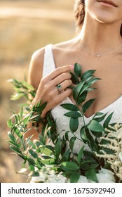 Close-up photo of wedding details with green flowers. Beautiful bride with thin fingers in minimalistic jewelry with engagement ring touches her flowers.
