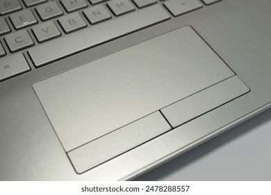 A close-up photo of a wide touchpad or trackpad and functional button area replacing mouse click and right-click on a thin silver laptop, showing a slight part of the space bar on the keyboard - Powered by Shutterstock