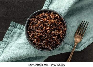 A closeup photo of wild black rice, shot from above on a black background with a fork