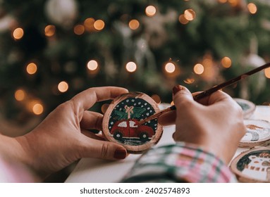 Close-up photo of woman crafting christmas ornaments, painting on a slice of wood.