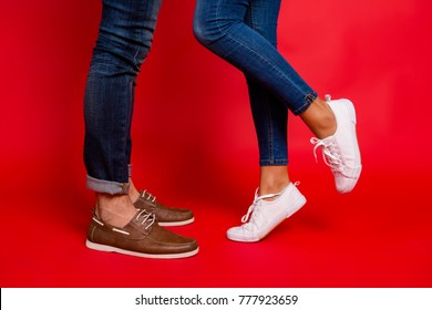 Closeup photo of woman and man legs in jeans, pants and shoes, girl with raised leg, stylish couple kissing during date, isolated over red background, he vs she