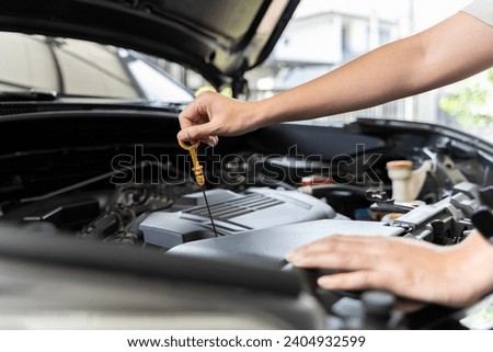 Close-up photo of woman's hand check engine oil A woman pulls out the dipstick to check the oil level of her car. Woman repairing car in garage or workshop Work and repairs at home.