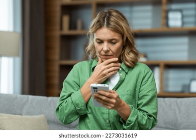 Close-up photo. Worried senior woman mother sitting on sofa at home and holding phone. Worries about children, writes and sends messages, calls, searches, waits at home. - Powered by Shutterstock