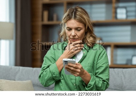 Close-up photo. Worried senior woman mother sitting on sofa at home and holding phone. Worries about children, writes and sends messages, calls, searches, waits at home.