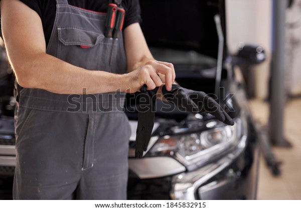 close-up photo of young auto service worker\
wearing black gloves, he is going to repair a car, opened hood of\
auto in the background