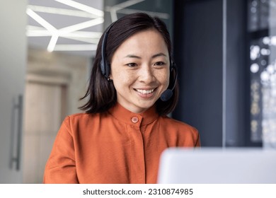 Close-up photo of young beautiful Asian woman talking on video call, looking at laptop web camera and smiling using headset for communication, successful businesswoman working in office. - Powered by Shutterstock