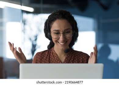 Close-up photo of young beautiful curly Arab woman talking on video call, looking at laptop web camera and smiling using headset for communication, successful businesswoman working in office - Shutterstock ID 2190664877