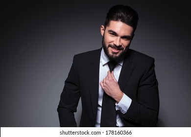 closeup photo of a young fashion man smiling for the camera while adjusting his tie. on a dark background