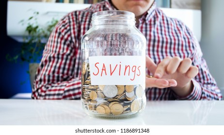 Closeup Photo Of Young Greedy Man With Jar Full Of Money Counting Coins On Hand