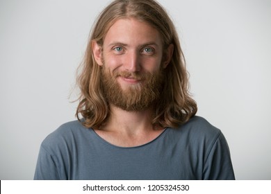 Closeup photo of young guy with a beard, blond hair to the shoulders and blue eyes looking happy one corner of the lips is raised in a smile, isolated over white background. - Powered by Shutterstock