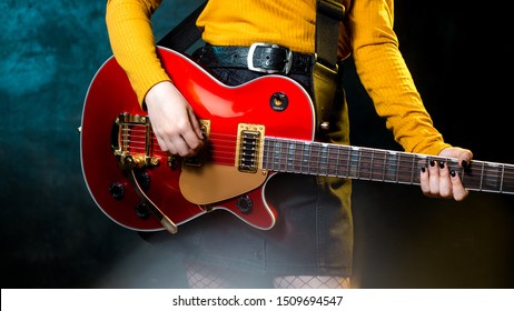 Close-up photo of young hipster woman legs and red guitar in neon lights. Rock musician is playing electrical guitar. 90s style concept.