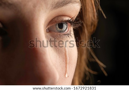 closeup photo of a young woman crying with a tear running down her cheek.