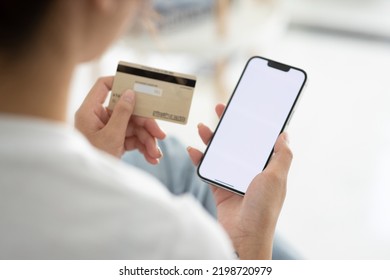A close-up photo of a young woman using her smartphone and her credit card at home. Online shopping ( credit card mockup ) - Shutterstock ID 2198720979