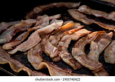 Close-up photograph of bacon being fried on a griddle.