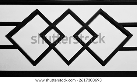 A close-up photograph of a decorative house fence featuring a symmetrical geometric pattern with intersecting diamond shapes. The design is modern and minimalist, with a strong black-and-white.