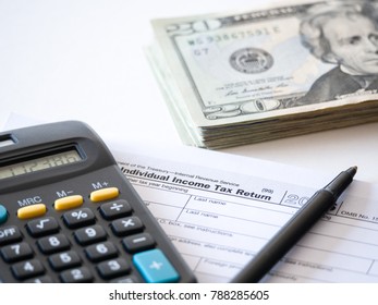 Close-up photograph of a hard copy of an individual income tax return with black calculator and 20 dollar bills piled up representative of United States federal tax cuts and savings this year. 
