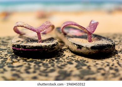 A close-up photograph of iconic sandy Australian thongs with blurred beach and sea background.