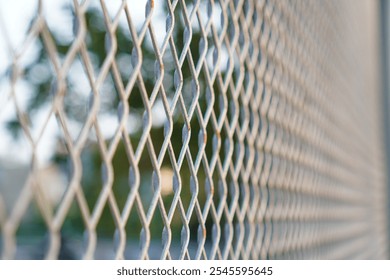 A close-up photograph of a metal fence, showcasing the intricate pattern and texture of the wire mesh. A close up of a metal fence The diamond pattern and blurry background create a sense of depth - Powered by Shutterstock