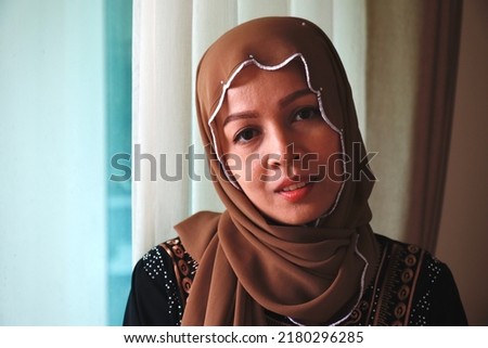 Close-up photograph of a mullim woman, wearing a brown hijab headdress, on halilaya day, islamic asian woman, Woman in traditional Muslim clothing, smiling. Beautiful woman headshot looking at camera 