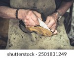 close-up photograph of old hands of an older shoemaker in a leather apron repairing shoes with glue. 