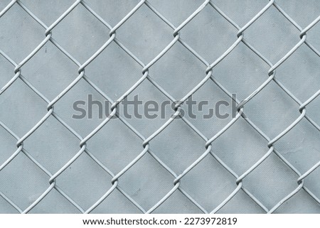 Closeup photograph of an old painted white and silver colored chainlink fence with crackled textured wind screen or tarp backdrop making a great background image.