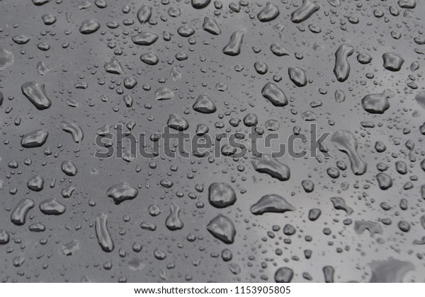 Closeup photograph of raindrops on\
the hood of a black car. Rain clouds are reflected in the\
hood.