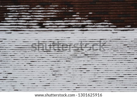 Closeup photograph of a roof partially covered with melting snow.