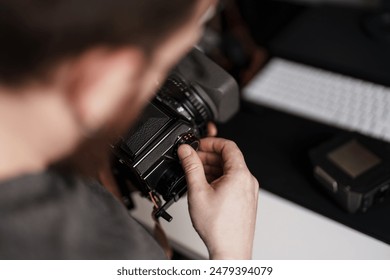 Close-up of a photographer focusing a retro camera before a photo shoot, with blurred background of office space. - Powered by Shutterstock