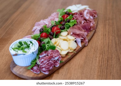 Close-up photography of assorted charcuterie board on a wooden surface, featuring a selection of cured meats, cheeses, fresh greens, cherry tomatoes, olives, and a creamy cheese spread. Stock Photo - Powered by Shutterstock