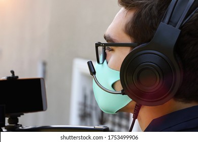 Closeup Photography Of A Videographer Working Outdoor,with Headphones And Microphone.Face Mask As Protection From Covid On The Face.