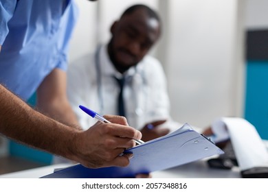Closeup of physician man nurse checking ill symptoms on clipboard discussing healthcare treatment with doctor working in hospital office. African american therapist analyzing medical documents