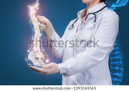A closeup of a physiotherapist with a stethoscope operating with a spine model with pelvis element with at dark background with digital spine image. A concept of spine diseases treatment.