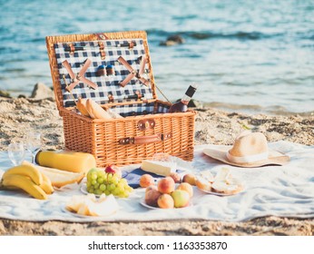 Closeup Of Picnic Basket With Drinks, Wine, Fruits On Sand Beach Near Sea