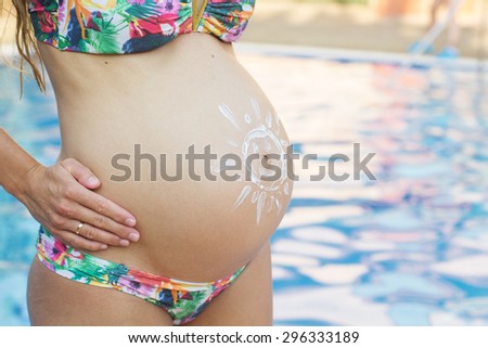 Closeup picture of belly of pregnant girl with sun picture over swimming pool with blue water