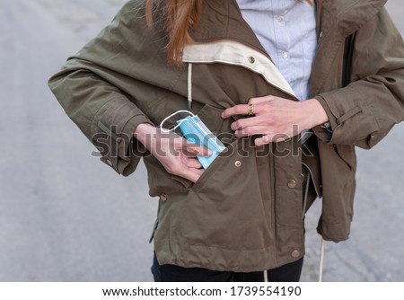 Closeup picture of a Caucasian girl's hands pulling surgical protective face mask out of her green pocket, concept for mask