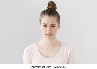 Closeup picture of nice young female without make up isolated on grey background raising eyebrow with vivid expression of suspicion, looking mistrustful towards she is hearing and looking at.
