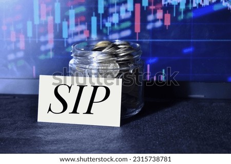 A closeup picture of a pot of coins with a label with text SIP against a candle and stick chart in the background