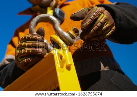 Closeup picture of rigger high risk worker wearing safety heavy duty glove, safety helmet fastening pin into D- shape shackle into crane lifting lug gate prior lift at construction site Perth city